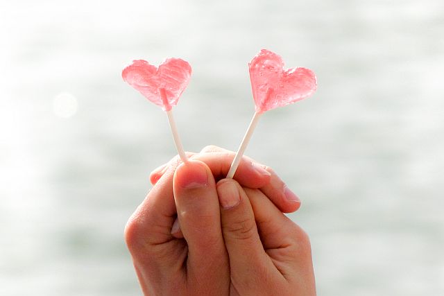 male and female hands holding heart-shaped lollipops 
