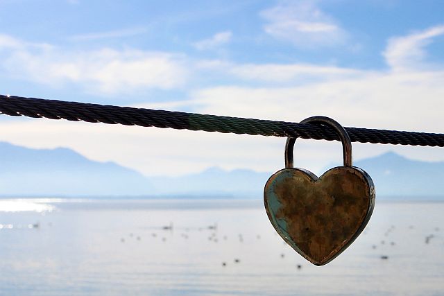 heart shaped lock on a cable in front of a seascape with mountains in the background