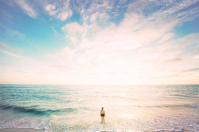 woman standing alone with feet in the water at the beach, looking out across the sea