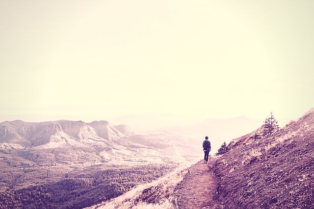woman walkingtowards the distance over a path in a wide mountainous landscape